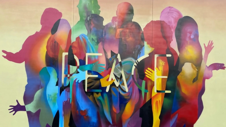 painted mural of rainbow colored sillouettes with the word "peace" centered 