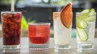 Close up of four glasses filled with ice and different drinks sit on a counter